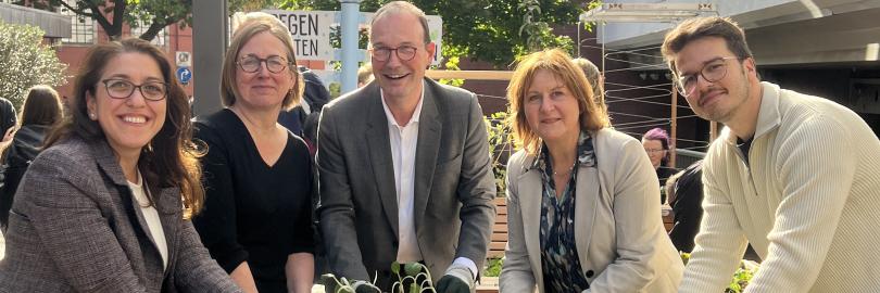 Verschiedene Personen stehen um ein Hochbeet und pflanzen gemeinsam.