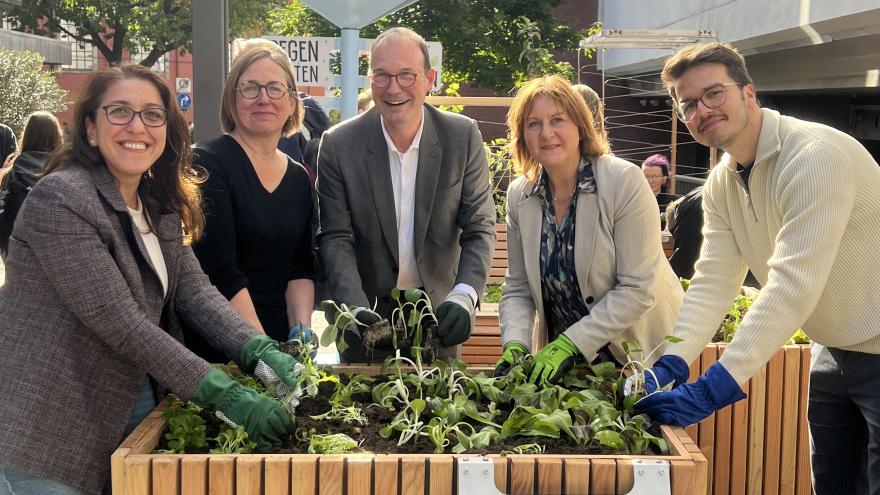 Verschiedene Personen stehen um ein Hochbeet und pflanzen gemeinsam.